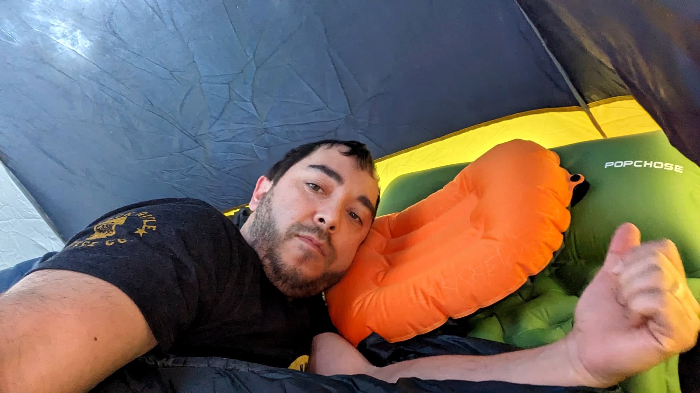A man lying in a tent on an inflatable sleeping pad with a small inflatable travel pillow