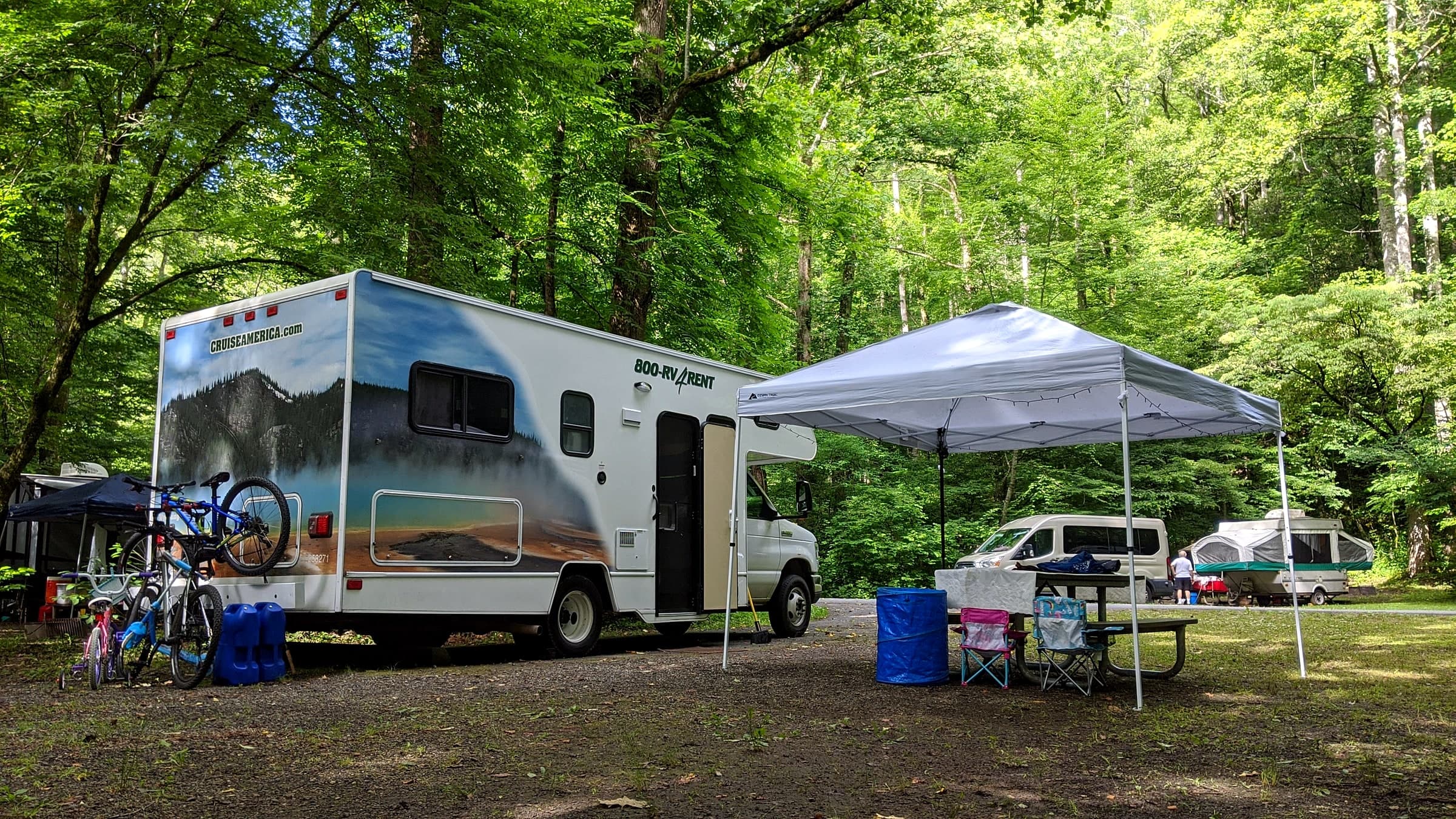 A rented Class C RV parked at a wooded campsite with bikes and a canopy set up outside