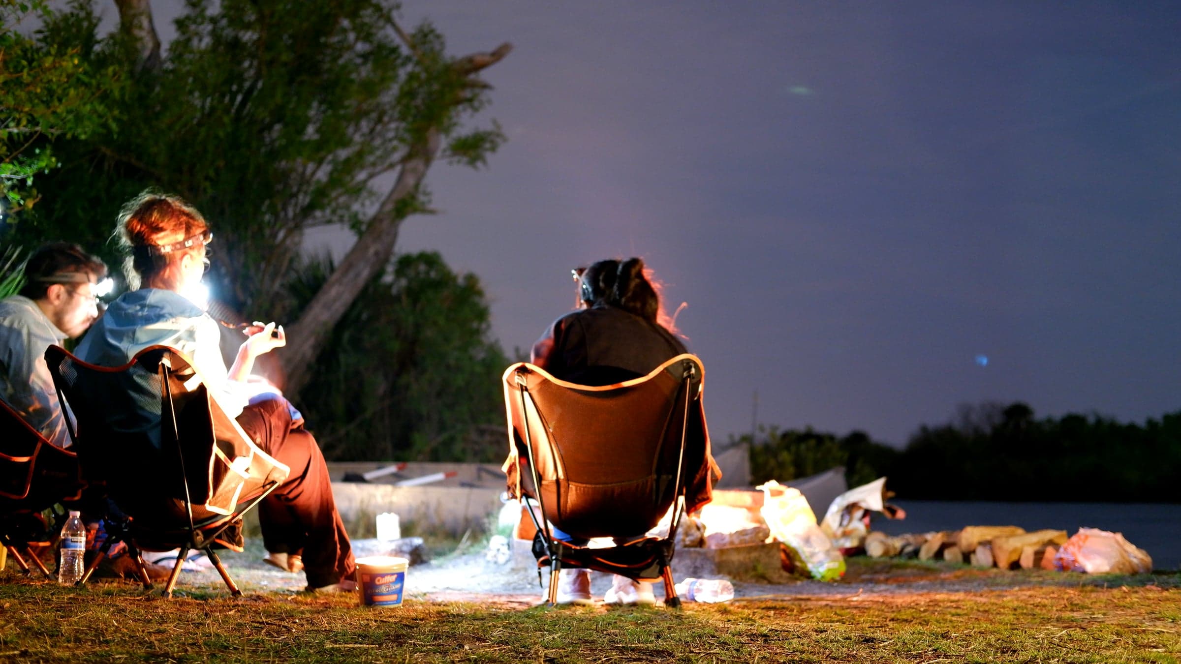 A dusk campsite at Canaveral National Seashore with two dome tents, string lights, a tarp shelter, and a canoe pulled up on the shoreline