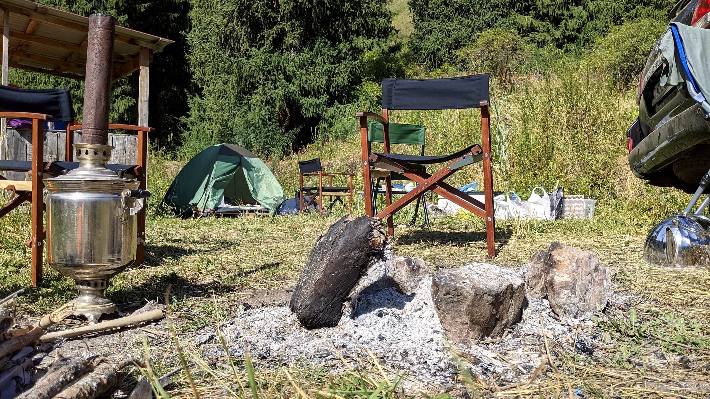 A samovar and tea kettle set over an open campfire at a forest campsite in Kazakhstan