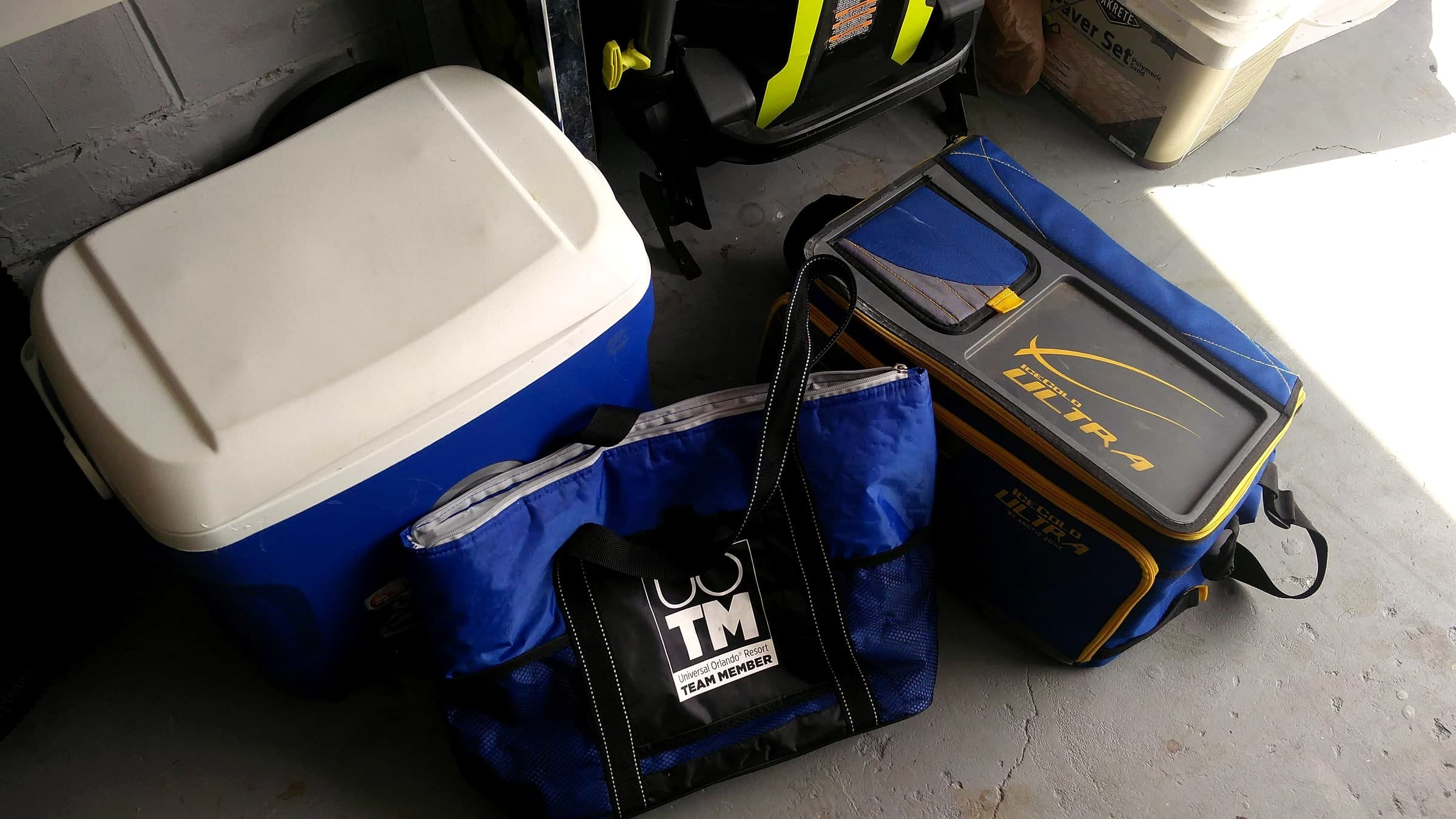 A stack of hard-sided and soft-sided coolers, including older Igloo and Coleman models, stored on a garage shelf