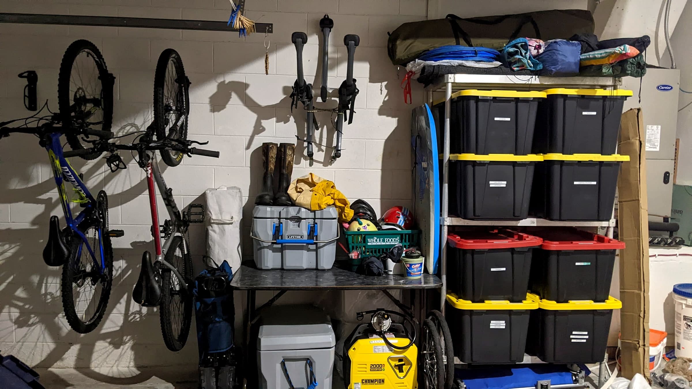 A garage shelf with labeled storage bins for camping, beach, fishing, and other gear categories, next to bikes and coolers