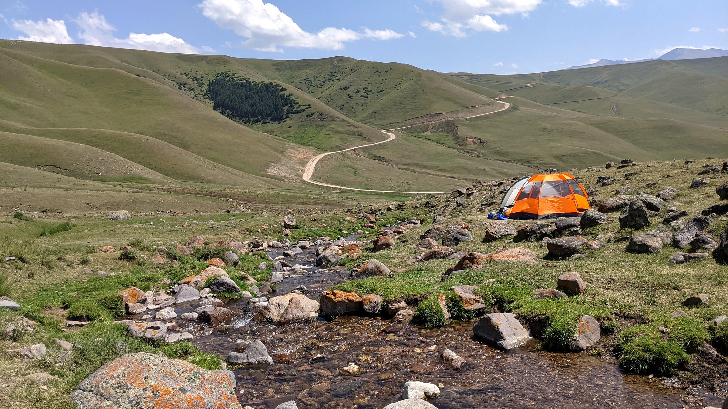 A backcountry tent set up in a mountain valley in Kazakhstan, with camping chairs nearby