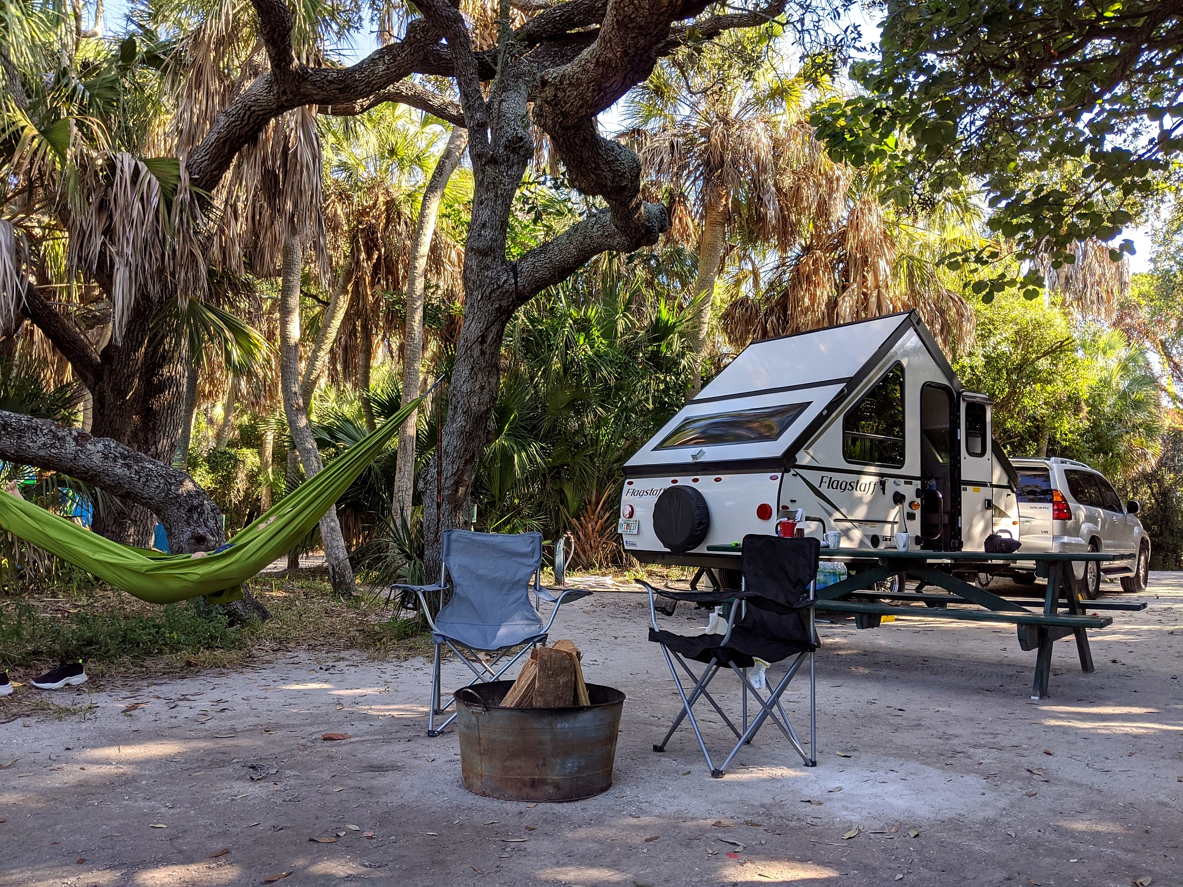 A Flagstaff pop-up trailer set up at a daytime campsite with camp chairs and a hammock nearby