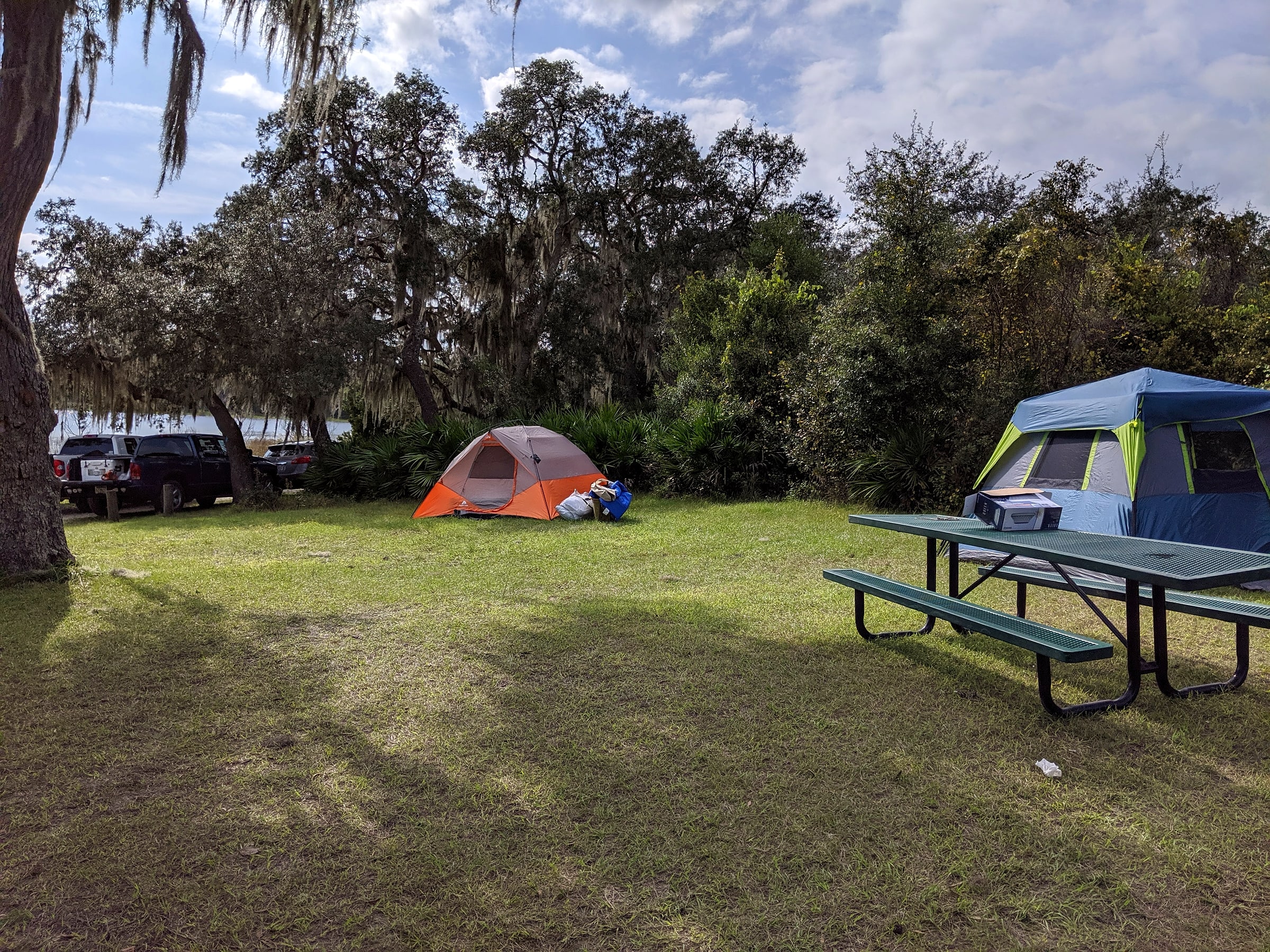 A blue and gray dome tent set up at a lakeside drive-up campground site under pine trees