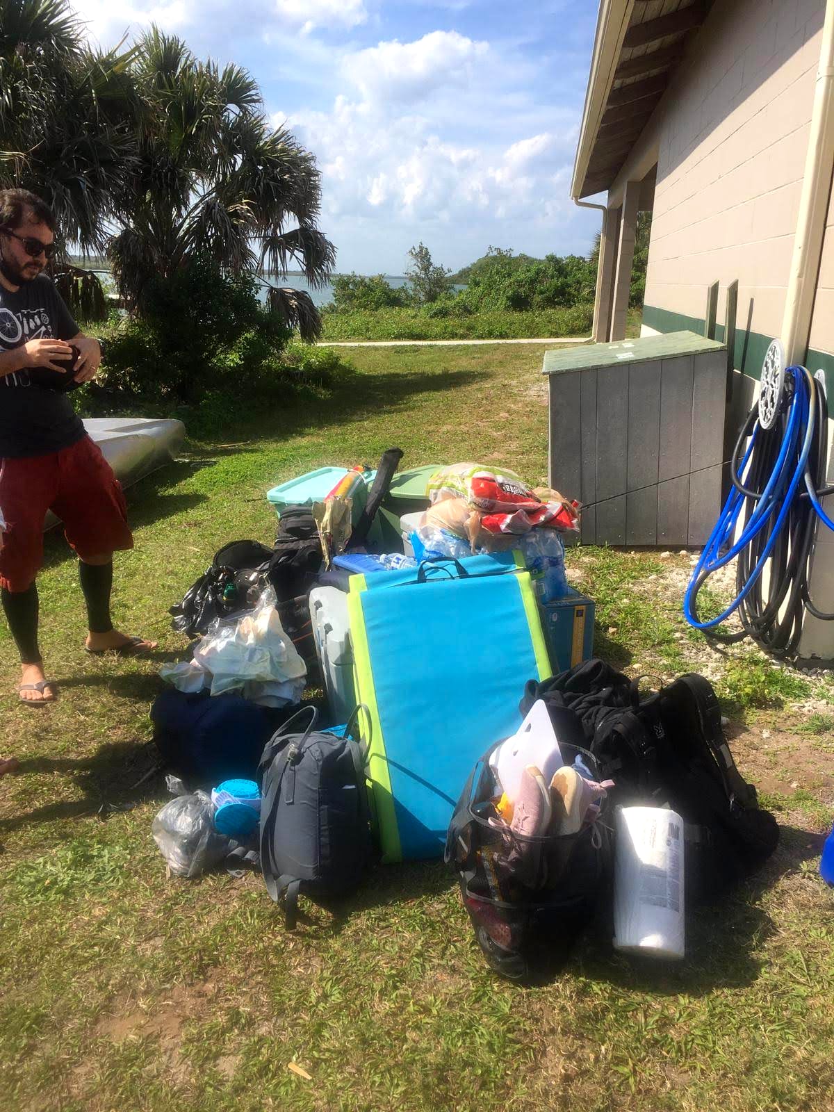 A pile of camping gear, coolers, dive bags, and a sleeping pad staged on the grass the morning after a canoe camping trip at Canaveral National Seashore