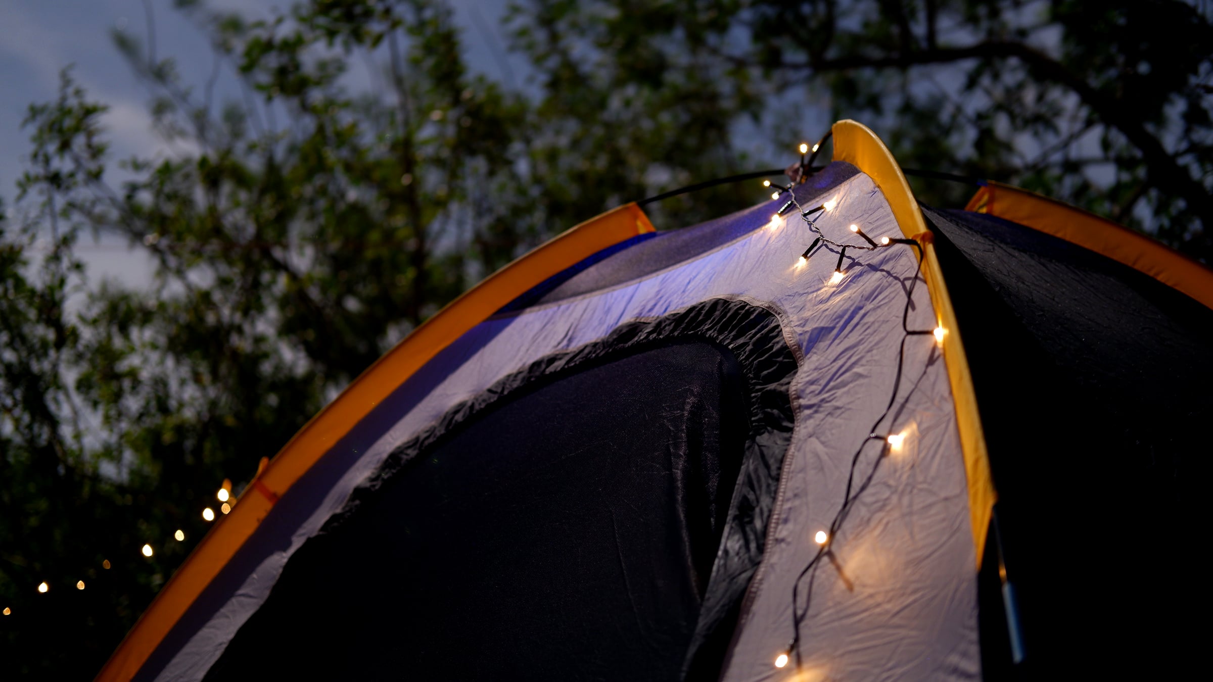 A tent glowing from string lights strung along its frame, photographed close-up at night at a Canaveral National Seashore campsite