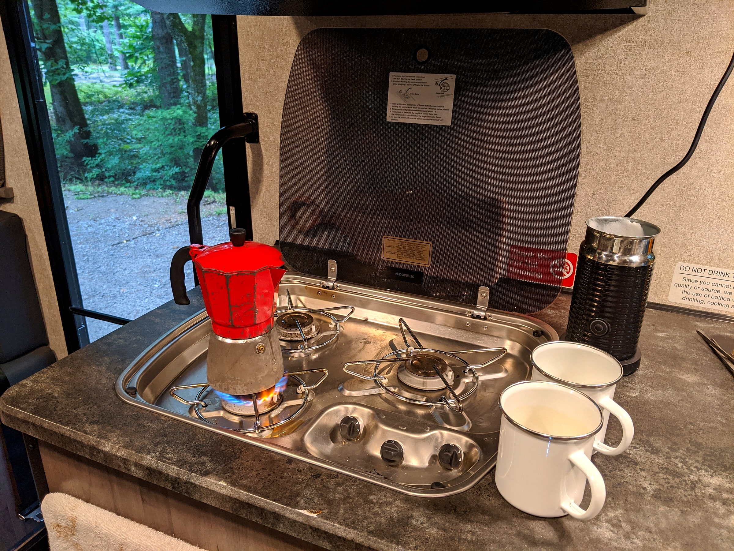 A moka pot and milk frother set up on a small stovetop inside an RV galley kitchen