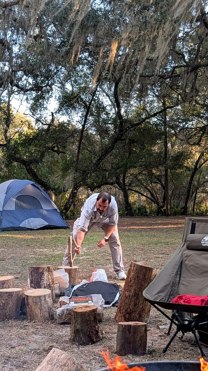 A child chopping firewood at a forested tent campsite