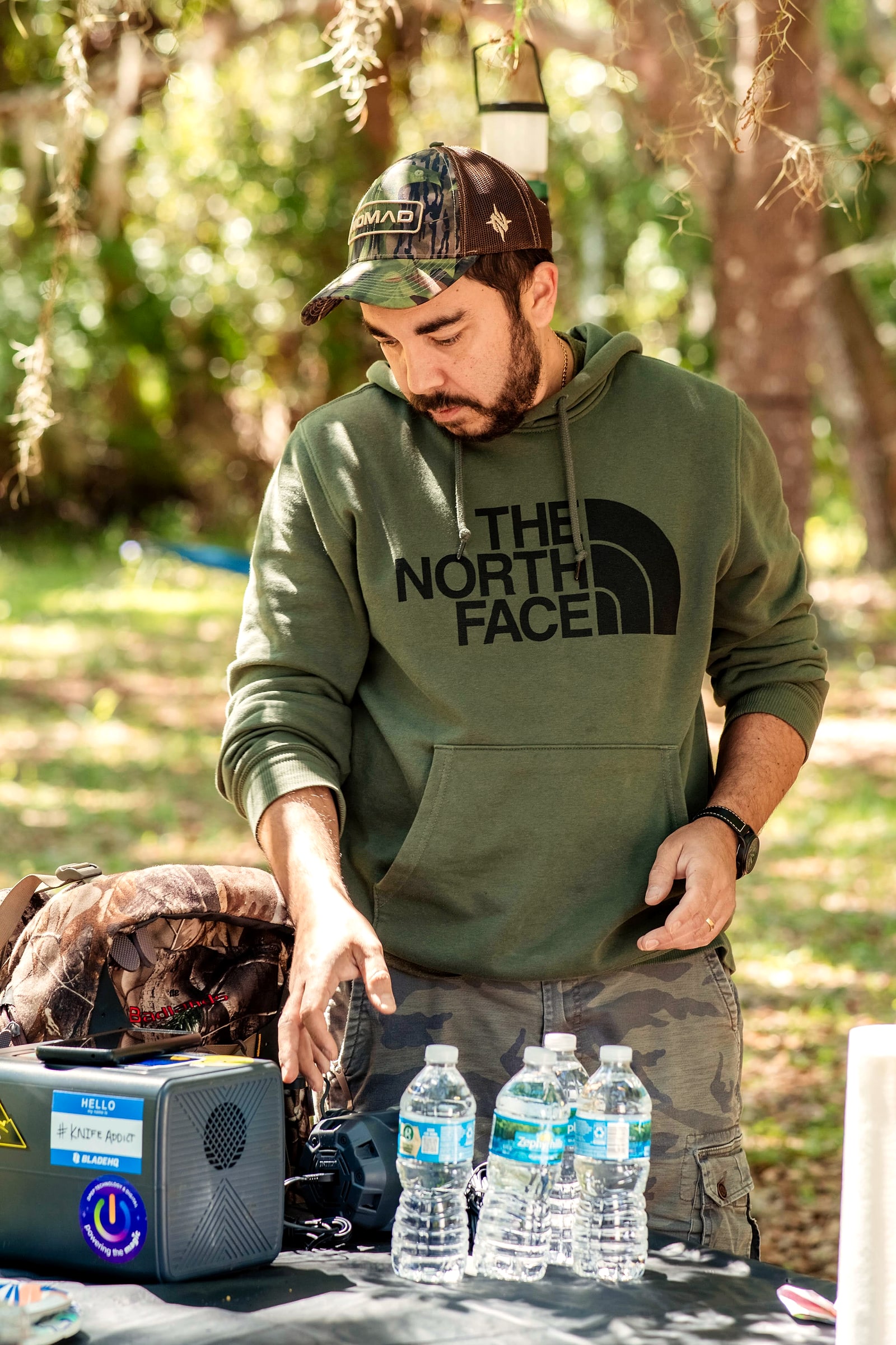 A man sitting at a campsite table next to a portable power station and water bottles