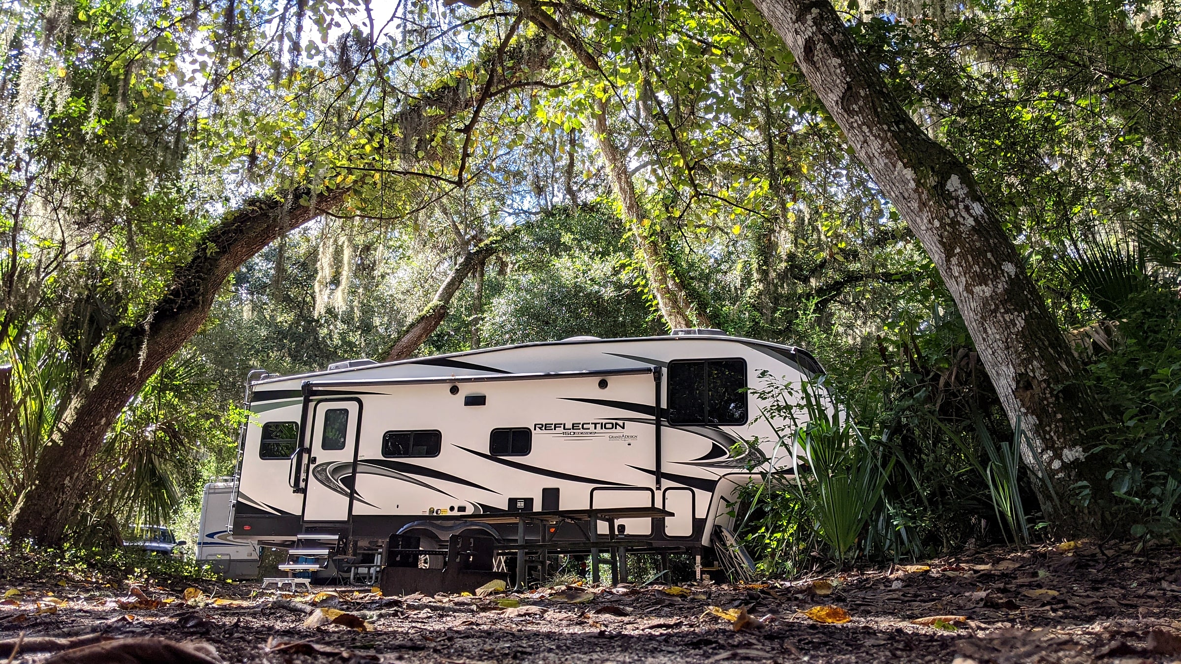 A rented fifth-wheel trailer parked under oak trees at a wooded Florida campsite, hitched to a truck