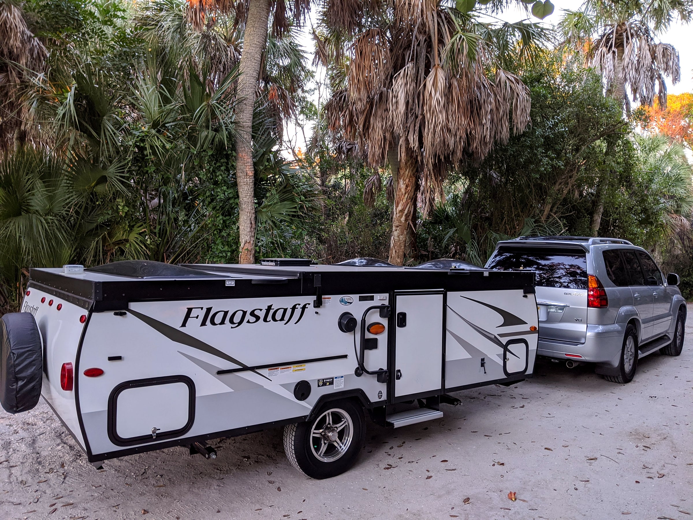 A Flagstaff pop-up trailer being towed by an SUV along a road with palm trees and a lake in the background